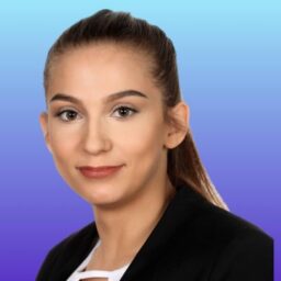 zdjęcie portretowe - bohaterka wywiadu, młoda kobieta patrzy przed siebie. Uśmiecha się. Ma długie, ciemne - zaczesane do tyłu włosy, odsłonięte uszy. Sylwetka uchwycona nieco z boku. Ma na sobie jasną bluzkę i ciemną marynarkę - z wycięciem w szpic