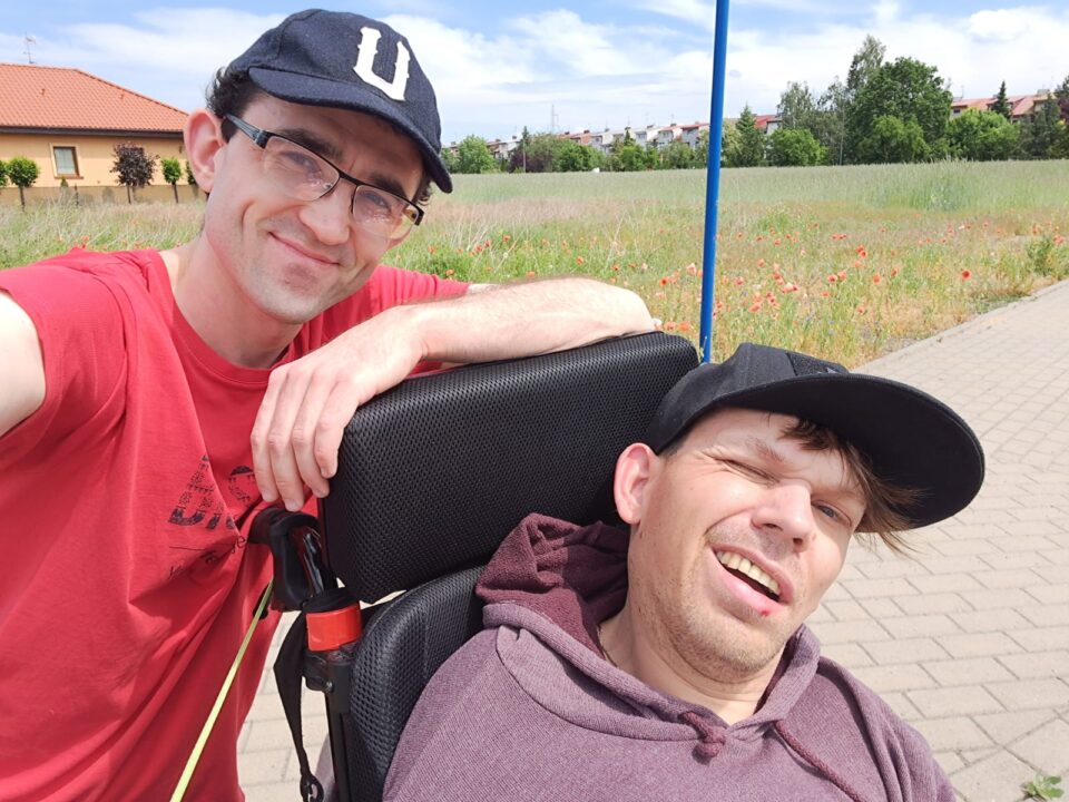 Zdjęcie asystenta z podopiecznym na wózku podczas spaceru. Zdjęcie wykonane w słoneczny dzień
